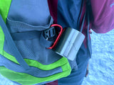 Metalltasse mit Karabiner-Griff hängt an grünem Rucksack