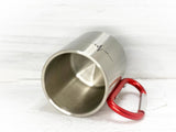 Liegende leere Metalltasse mit rotem Karabiner-Griff