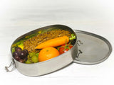 Ovale Brotbox aus Metall, gefüllt mit belegter Semmel, Obst und Gemüse 